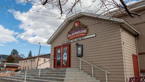 Historic playhouse building with a red door and community theater sign under a blue sky