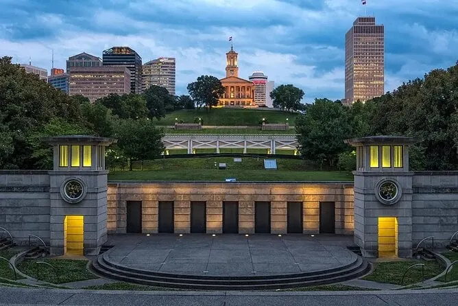 The Tennessee State Capitol lit on its hill at dusk above a terraced stone plaza, downtown office towers standing on either side