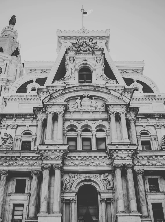 Low angle view of Philadelphia City Hall's carved stone facade in black and white, columns and statuary stacked toward a pale sky