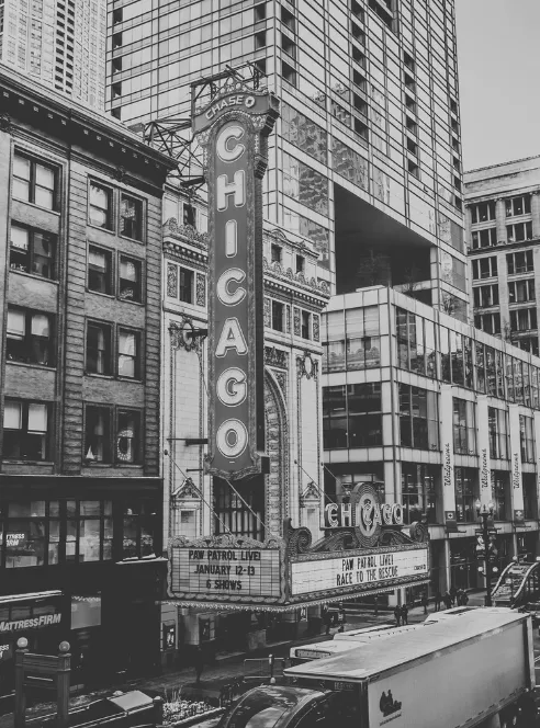 The Chicago Theatre's vertical marquee sign hangs over State Street in black and white, older brick storefronts crowded in beside it