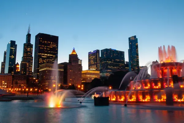 Buckingham Fountain lit orange against a blue dusk sky, the downtown skyline standing behind it