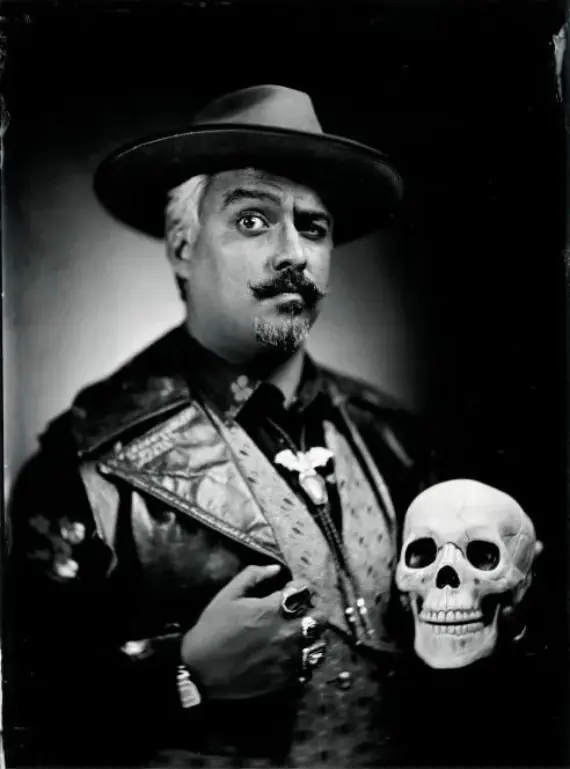 Tintype-style portrait of a man in a wide-brim hat holding a human skull