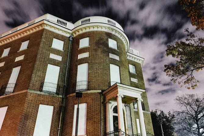 A brick townhouse shot from below at night, its rounded corner bay and white columned entry under a sky streaked with cloud