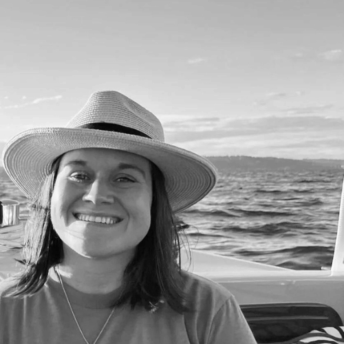 Black-and-white portrait of a smiling woman in a sun hat on a boat over water