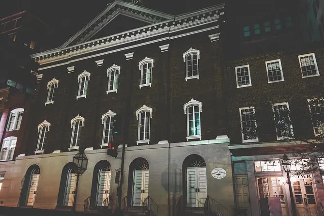 A brick building lit at night, five arched doorways at street level under two rows of white-trimmed windows, an iron lantern on the wall beside the entrance