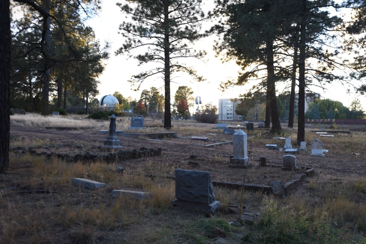 Weathered headstones and stone markers catch the last light in Flagstaff's Citizens Cemetery, an observatory dome peeking through the ponderosas beyond.