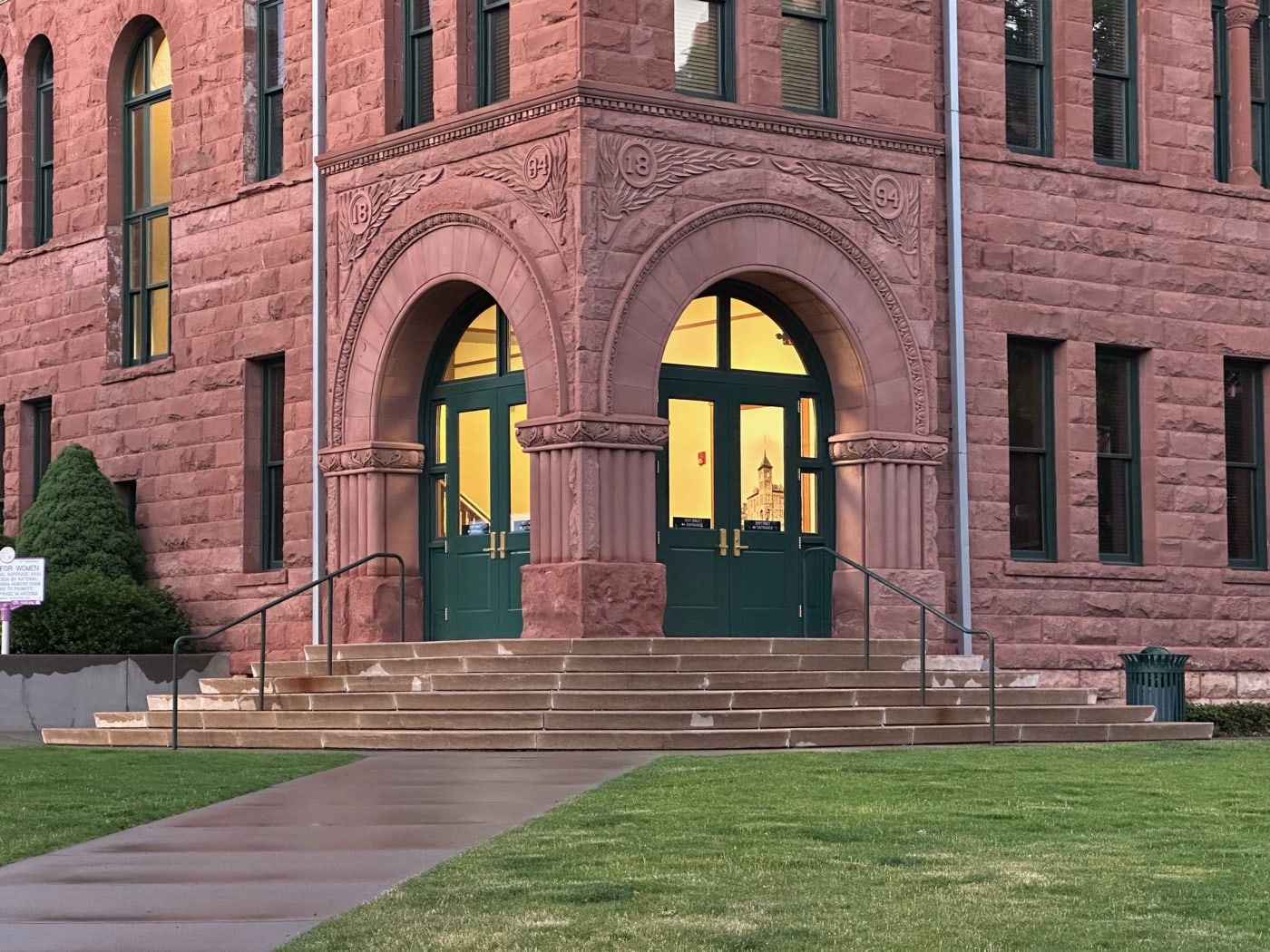 Sunset turns the 1894 red sandstone courthouse to ember tones while its green double doors glow like lanterns for the evening walk.