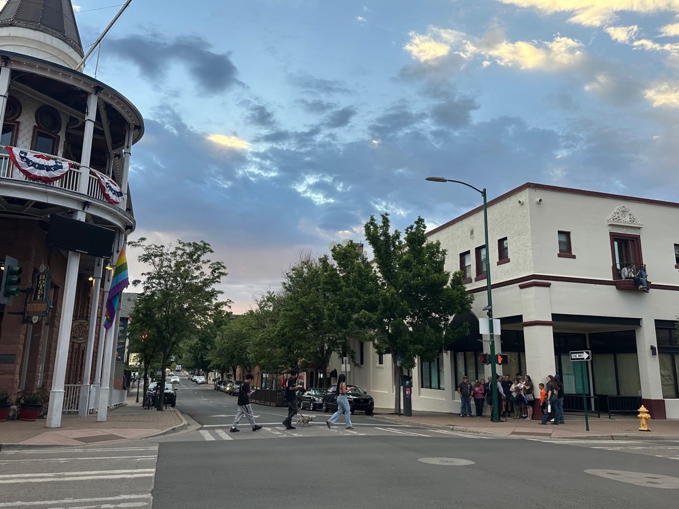 Sunset clouds break over downtown Flagstaff as walkers cross Leroux Street beside the Weatherford Hotel's century-old balcony and bunting.