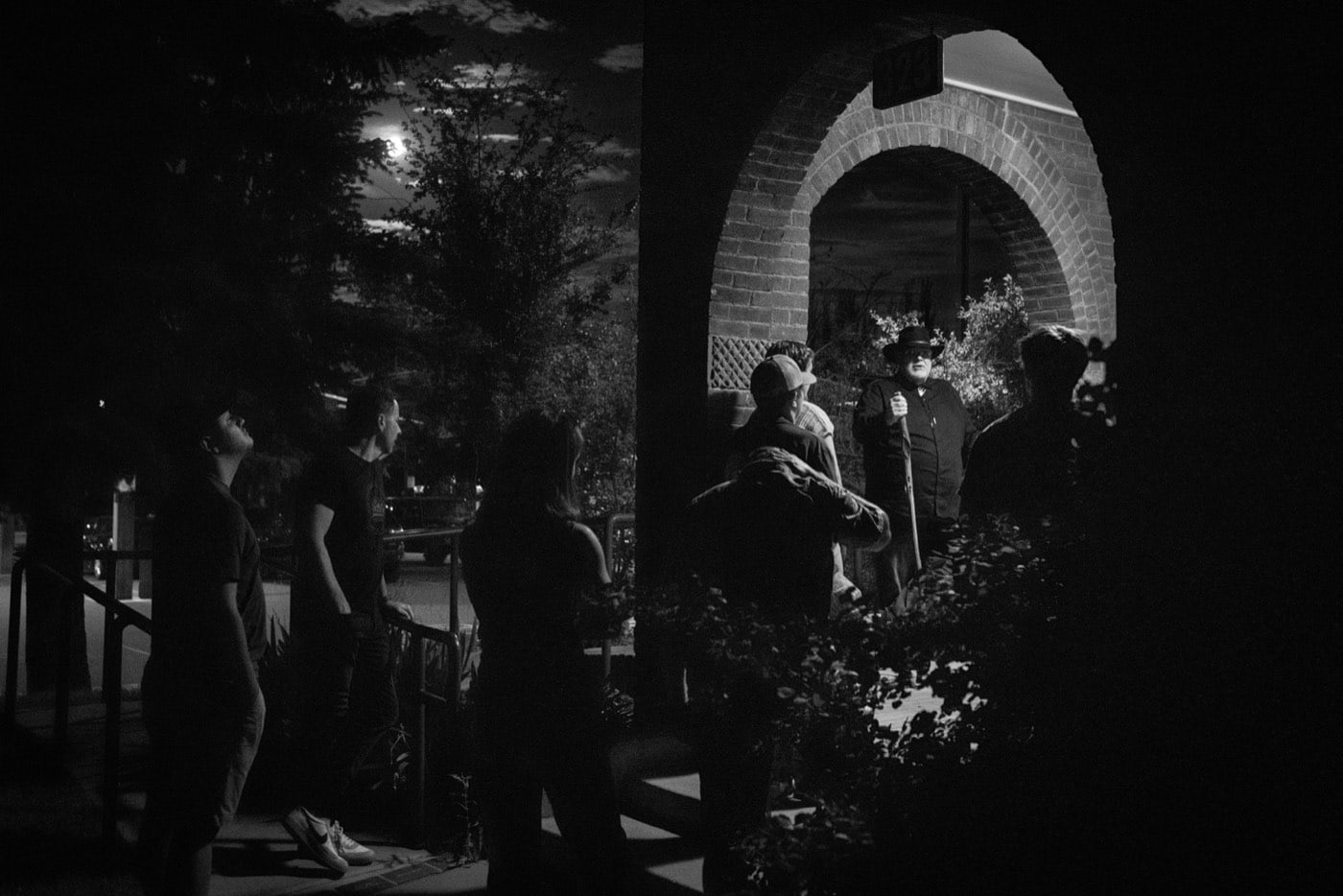 Under a full moon, the guide pauses beneath the brick archway of the night tour's Victorian house stop while guests hang on every word.
