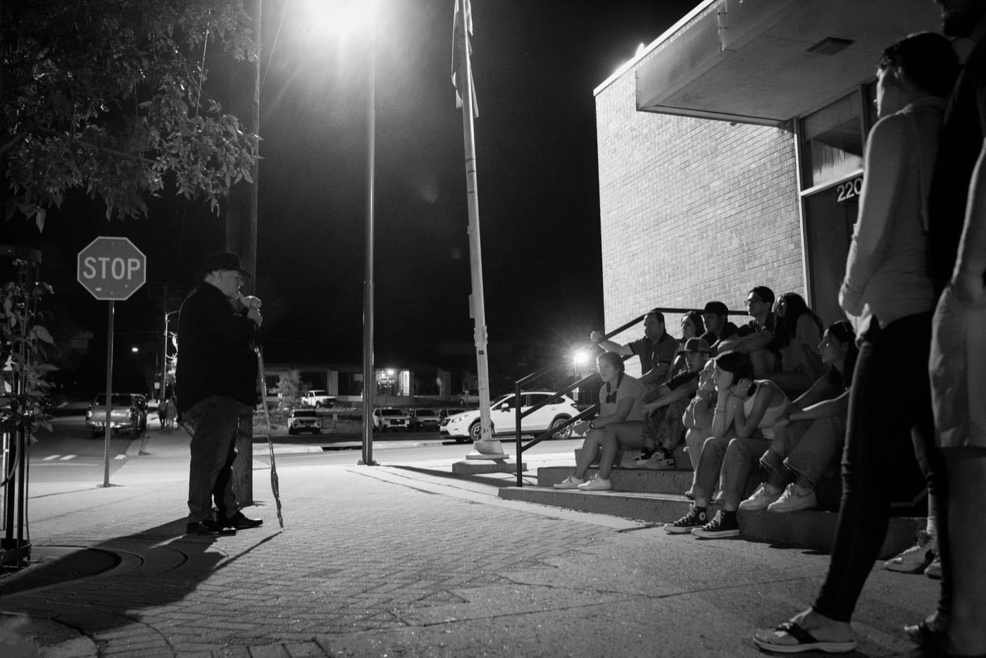 Seated on cool concrete steps, guests lean in as the guide's cane taps out the rhythm of another downtown legend.