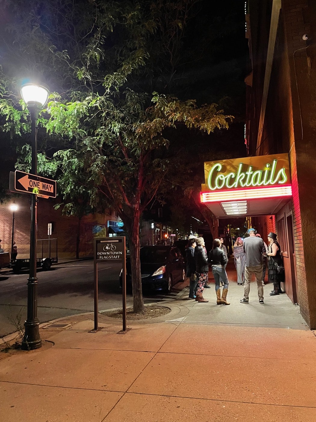 Lamplight and the Monte Vista Lounge's Cocktails neon light a quiet downtown Flagstaff corner as a night tour group clusters at the door of the haunted 1927 hotel's bar.