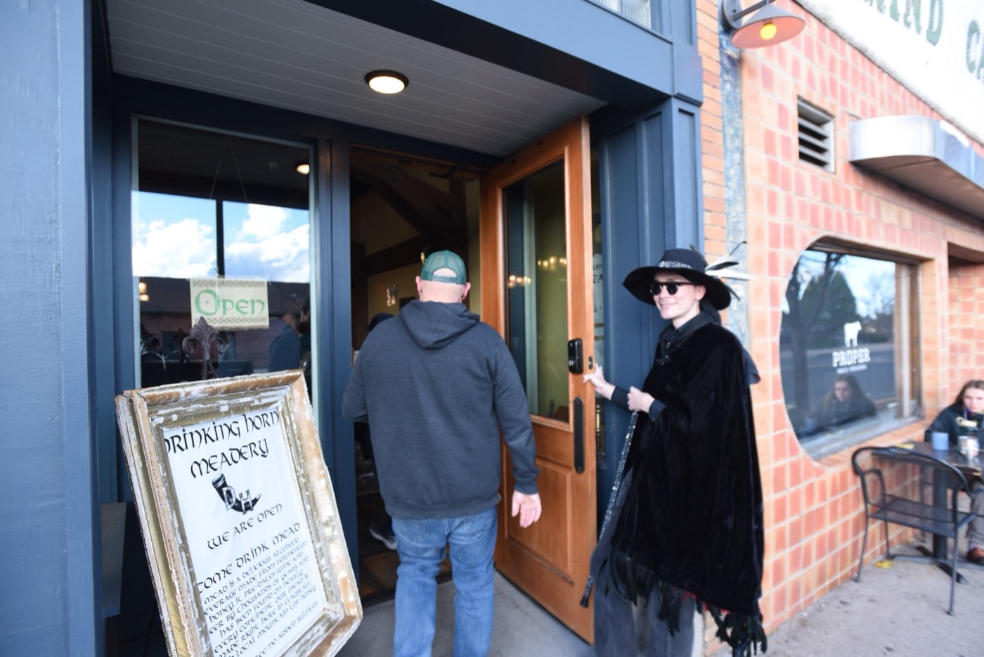 Holding the door in full witchy black, a Freaky Foot Tours guide ushers a guest past the Drinking Horn Meadery welcome board on the adults-only Spirits With The Spirits pub crawl in Flagstaff.