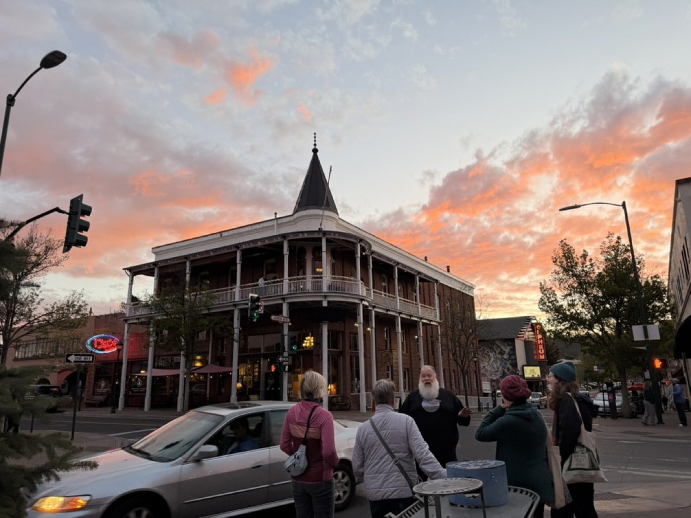 An orange sunset flares over the Weatherford Hotel's 1900 cupola while a Freaky Foot Tours guide talks Route 66 history with guests across Aspen Avenue.
