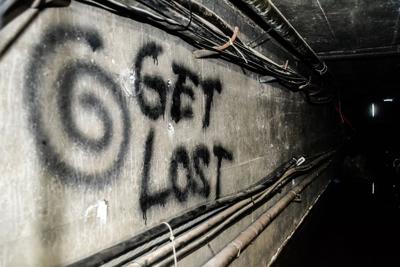 Spiral graffiti reading get lost spray-painted on a dark utility tunnel wall