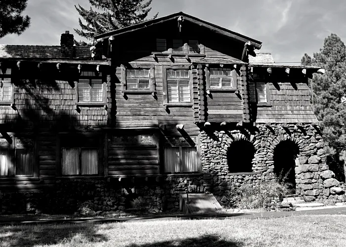 Black-and-white log-and-stone lodge with deep eaves among tall pines