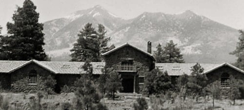 Vintage view of a low stone Craftsman mansion below the San Francisco Peaks