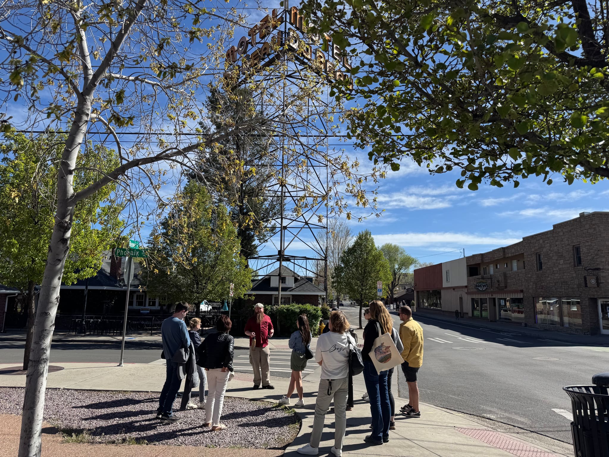A tour group listens to their guide beneath the Motel Du Beau sign tower in Flagstaff