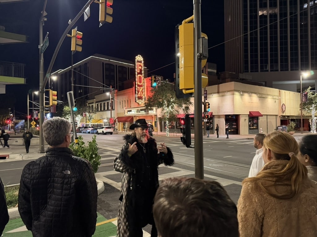 A costumed guide tells a story to guests as the Fox Theatre neon glows on Congress Street in Tucson